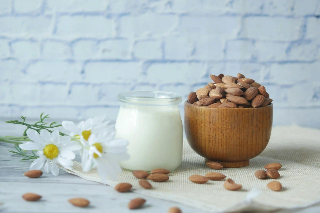 natural_almonds_in_a_wooden_bowl_with_a_glass_jar_of_milk_and_white_chamomile_flowers_on_a_wood_table